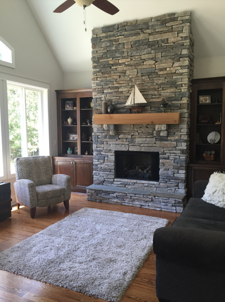 Living room with stone fireplace, built-in shelves, armchair, sofa, and a fluffy rug.