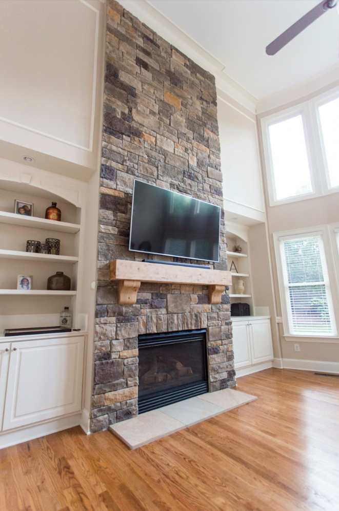 Stone fireplace with a mounted TV, flanked by built-in white bookshelves in a living room.