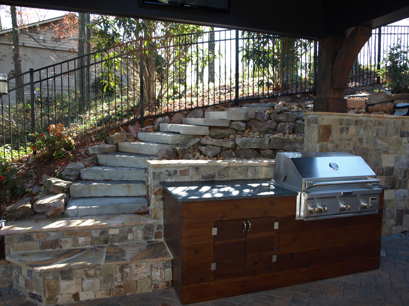 Outdoor kitchen with built-in grill, stone steps, and wooden cabinetry.
