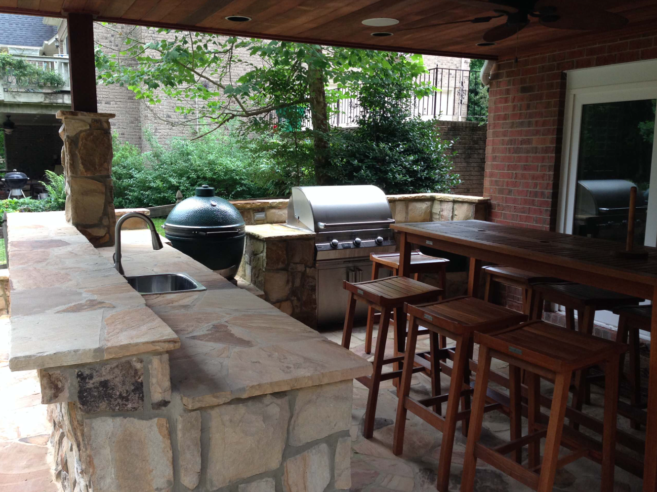 Outdoor kitchen with a grill, sink, and bar seating under a covered patio.