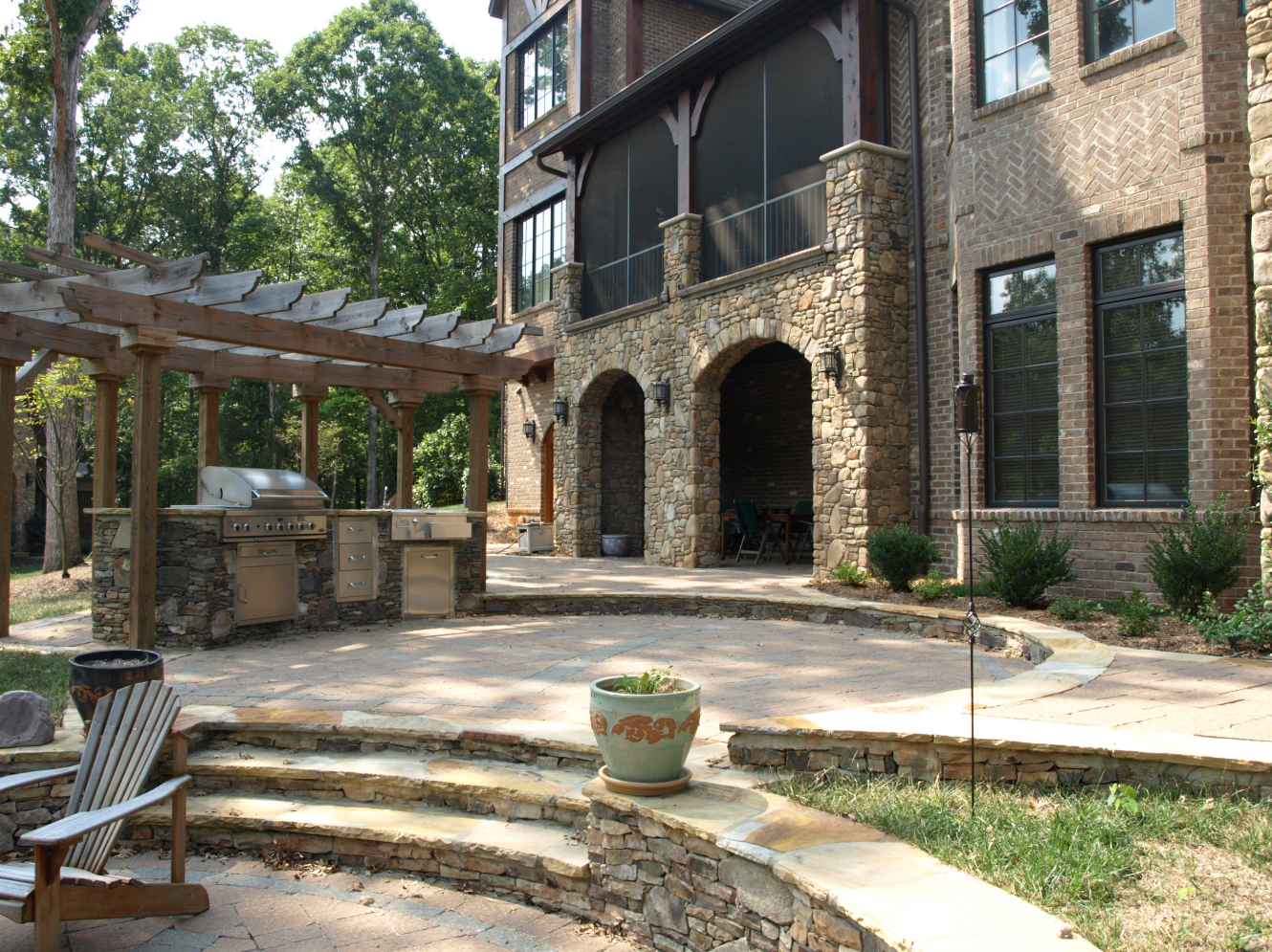 Backyard patio with stone walls, grill, pergola, and two-story brick house.