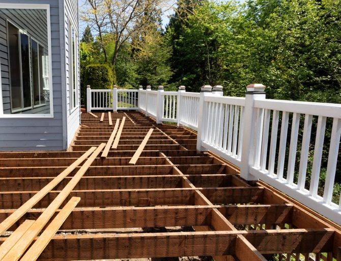 Partially built wooden deck beside a house, with white railing and exposed joists in a sunny yard
