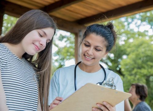 A nurse is talking to a young girl while holding a clipboard.