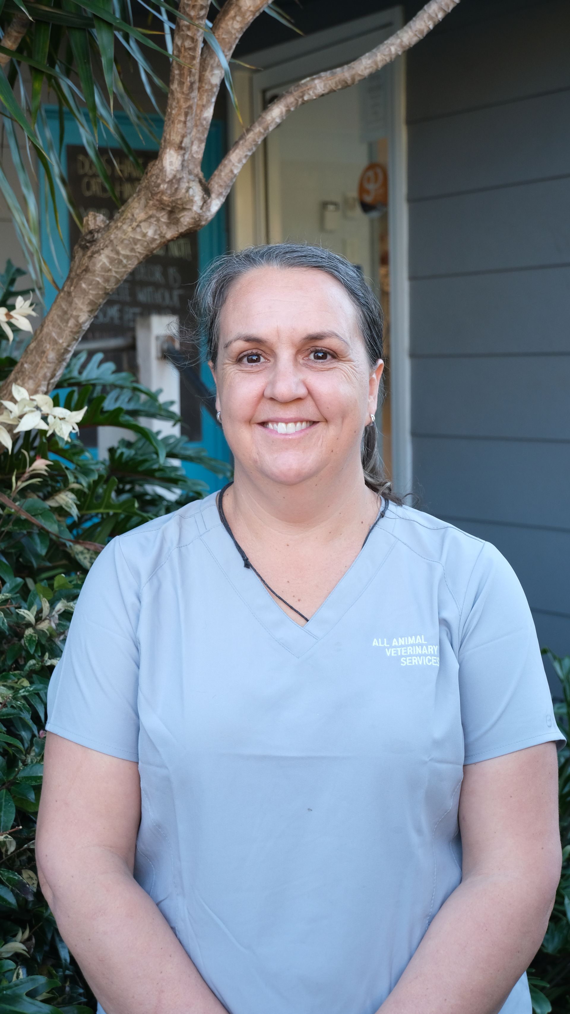 A woman in a scrub top is standing in front of a tree.