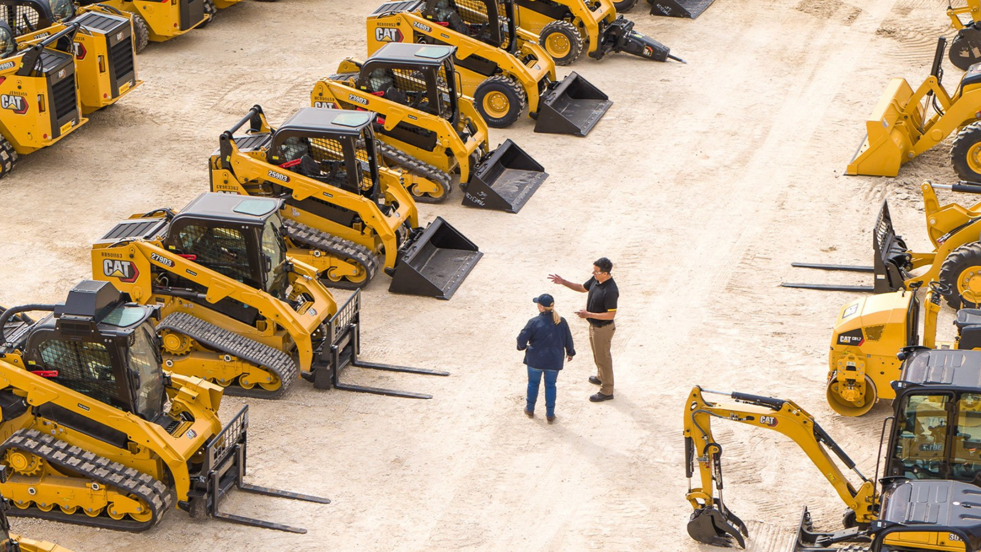 Two men are standing in front of a row of construction vehicles.