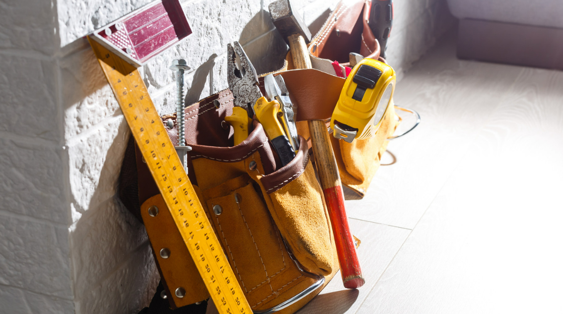 A tool belt filled with tools is leaning against a wall.