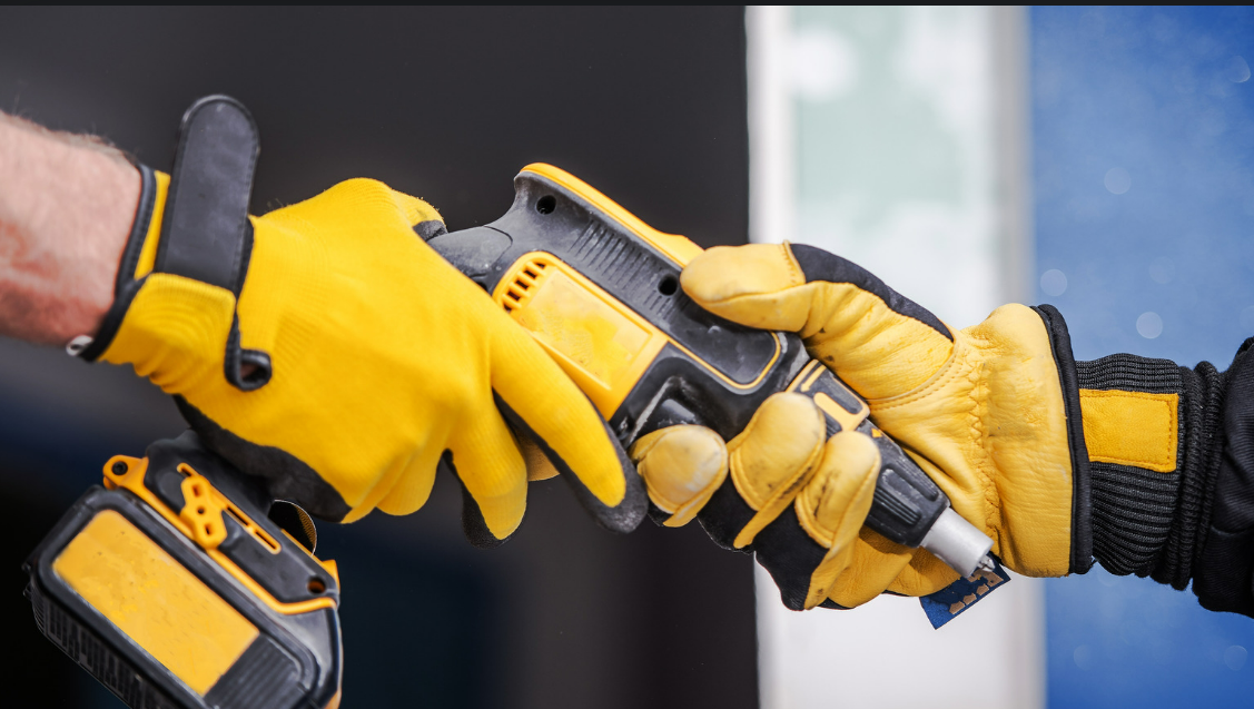 A person wearing yellow gloves is holding a drill in their hand.