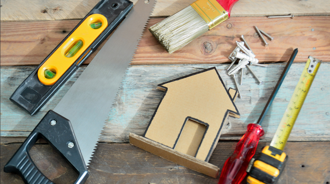 A wooden table topped with tools and a cardboard house.
