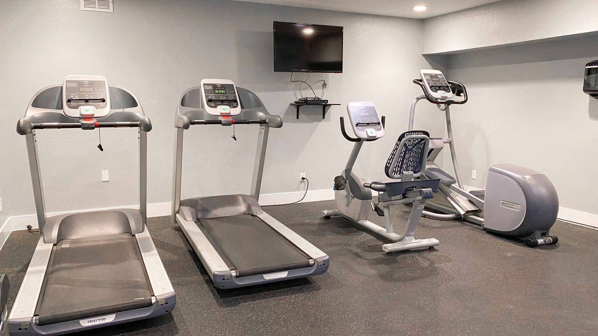 a gym with treadmills , bikes , and a flat screen tv .