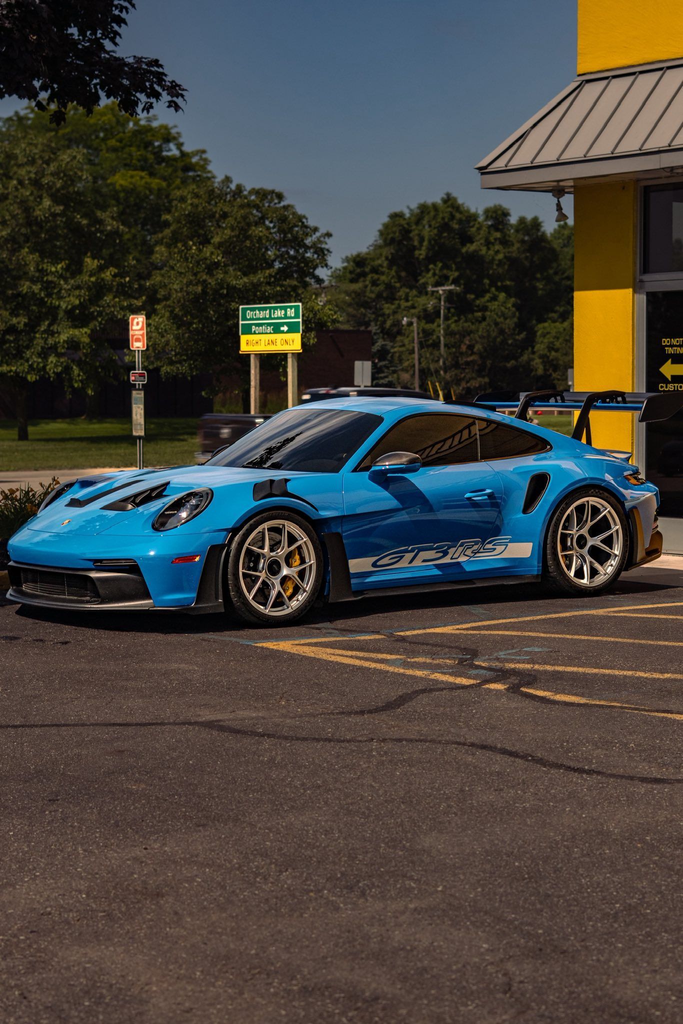 Bright blue sports car parked outside a building, with gold wheels and a black roof.