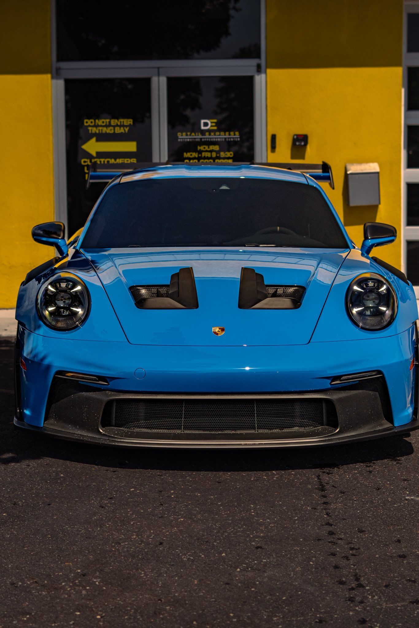 Blue Porsche sports car parked in front of a yellow building at night