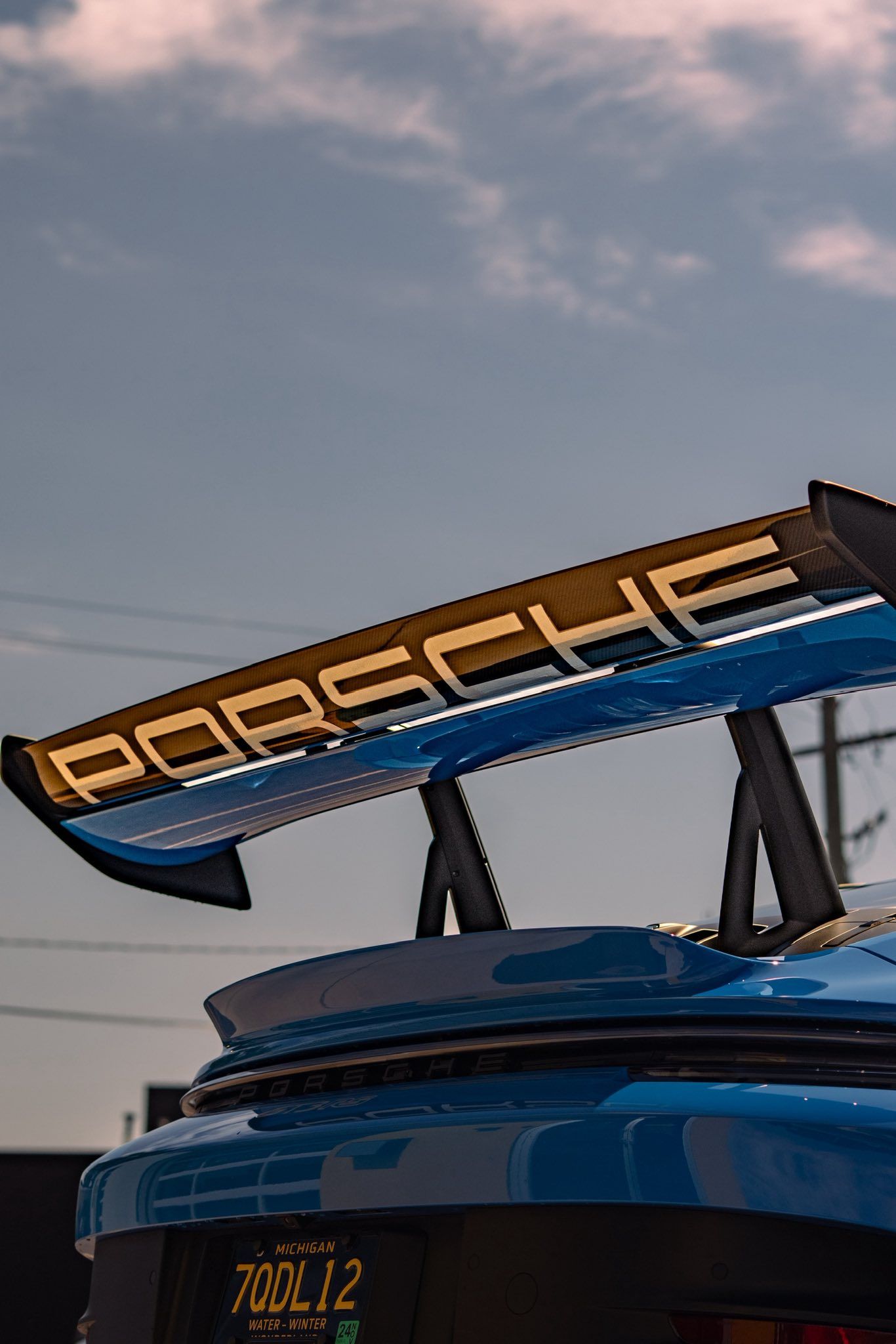 Close-up of a blue Porsche race car’s rear wing and spoiler against a cloudy sky