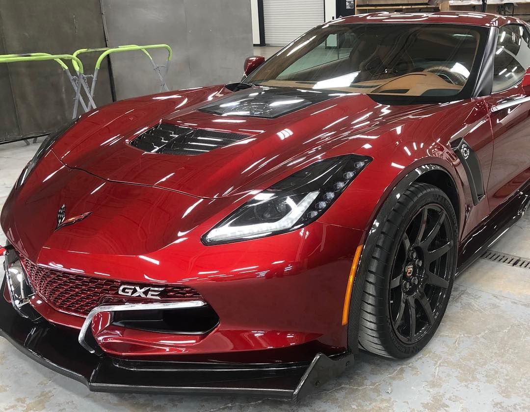 Red sports car with black wheels parked indoors, front-left view.