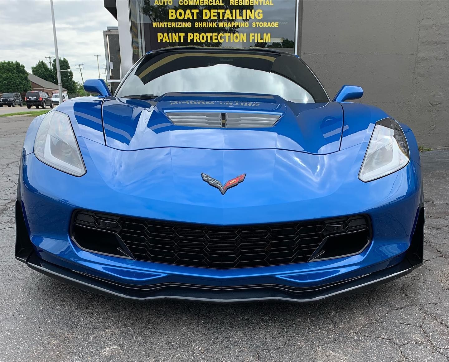 Blue Chevrolet Corvette sports car parked outdoors, front view with a windshield sign.