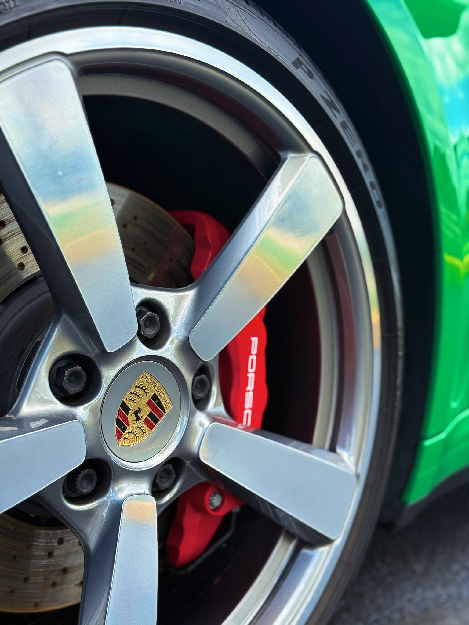 Close-up of a Porsche wheel with silver rim, red brake caliper, and green car body.