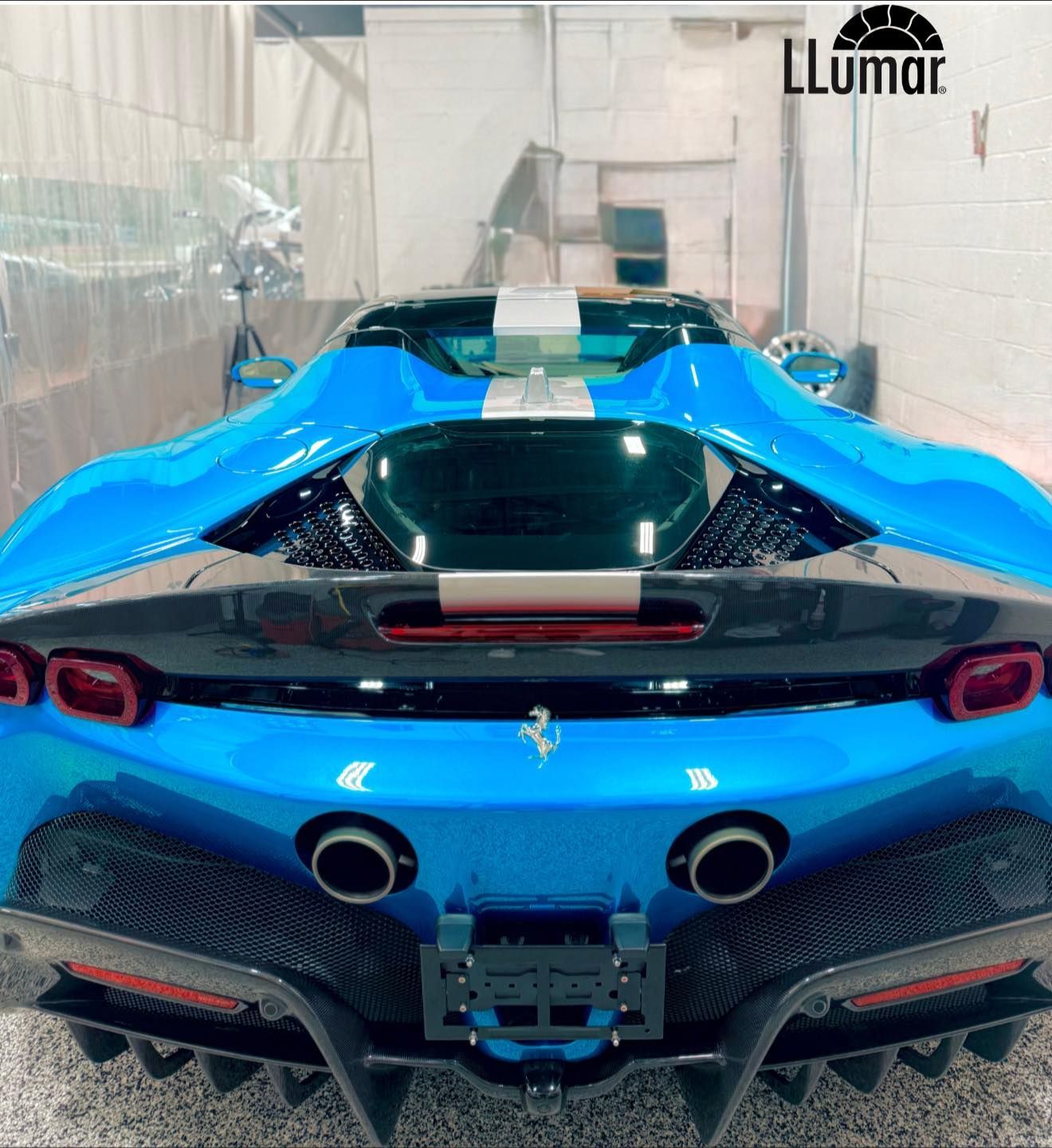Blue Ferrari sports car in a workshop, rear view with twin exhausts and a black carbon-fiber spoiler