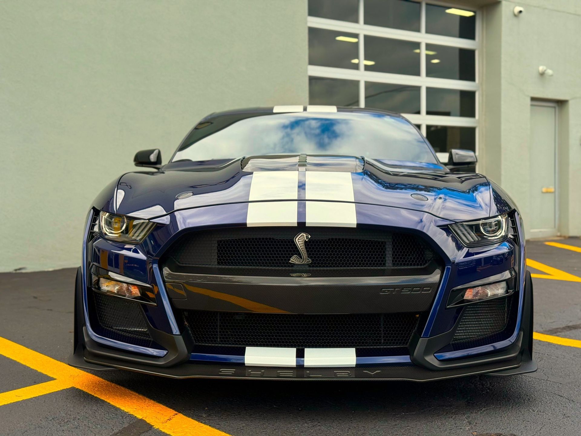 Blue sports car with white racing stripes parked outside a building