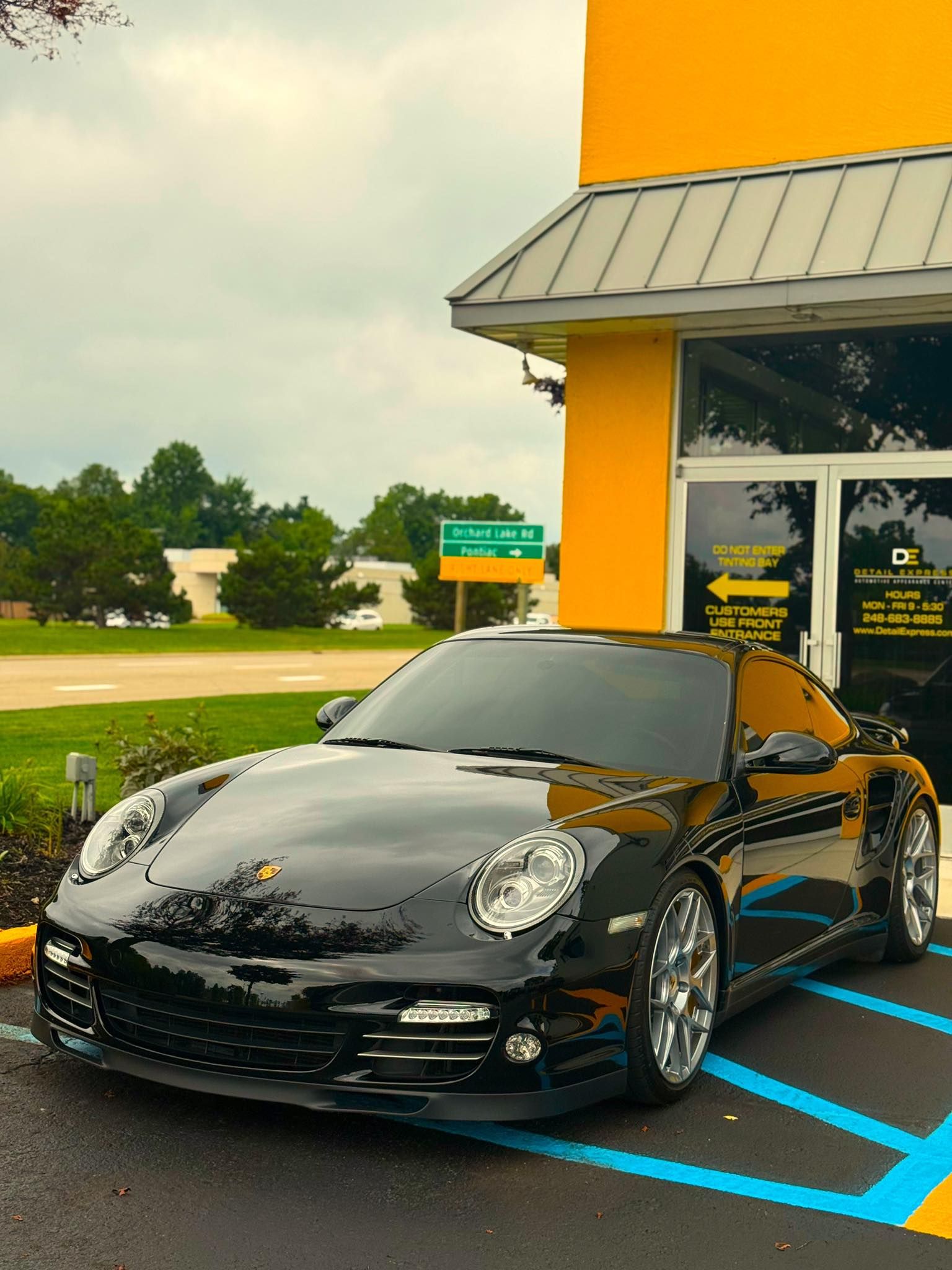 Black sports car parked outside a yellow building on a blue-striped accessible space