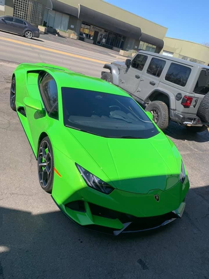 Bright green sports car parked in a lot beside a white Jeep, outside a beige building.