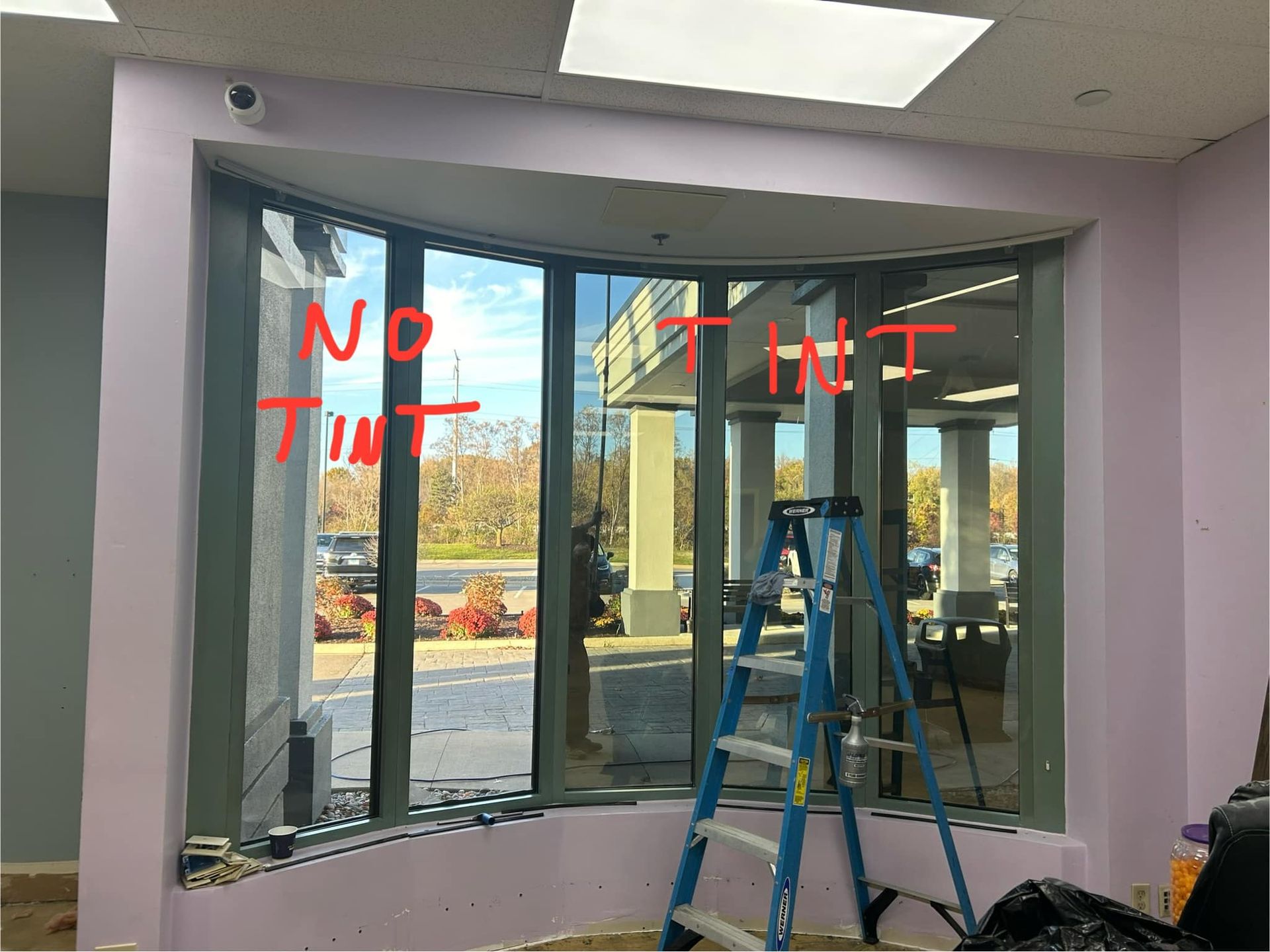 Interior under construction with a large curved window, red writing on glass, and a blue step ladder.