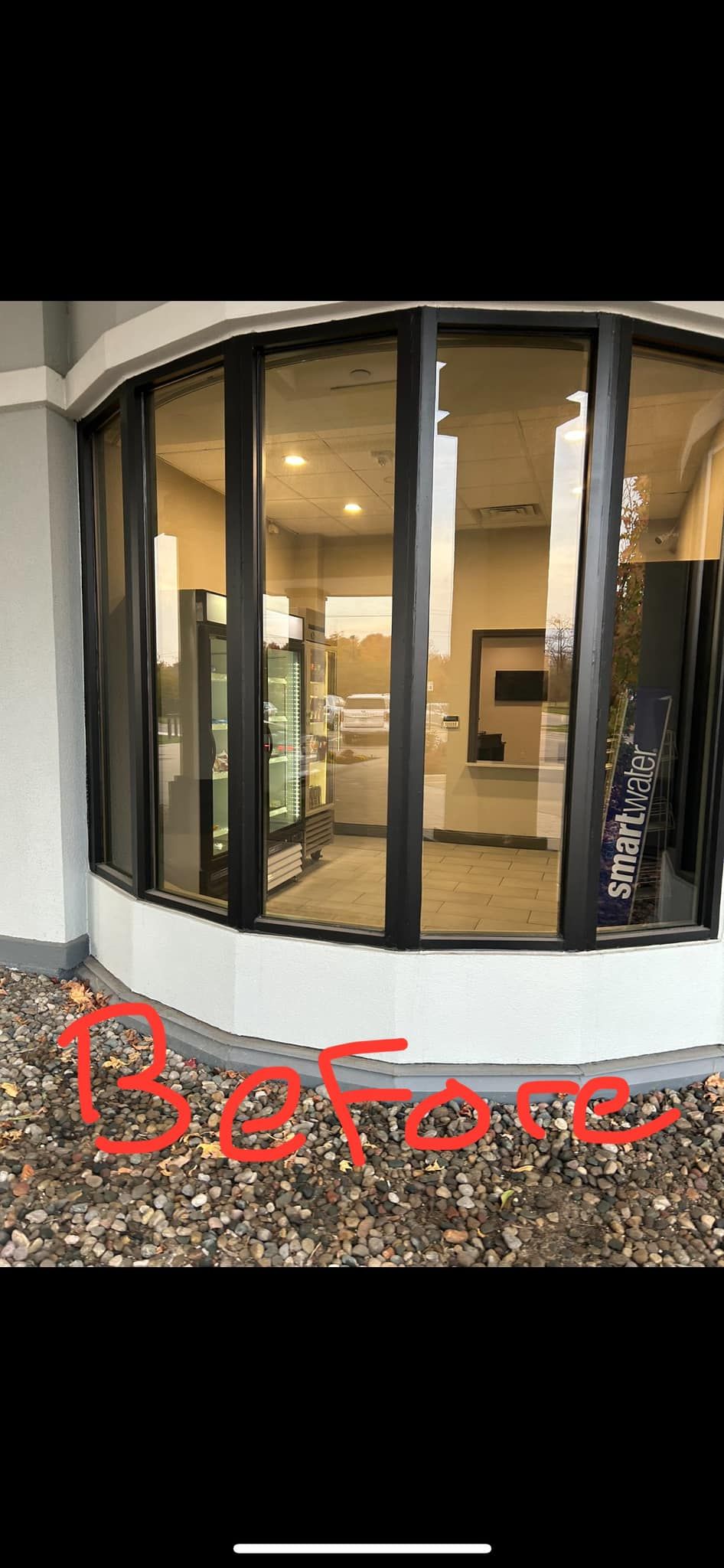 Curved glass storefront with red “Before” text on gravel foreground and interior lights visible inside