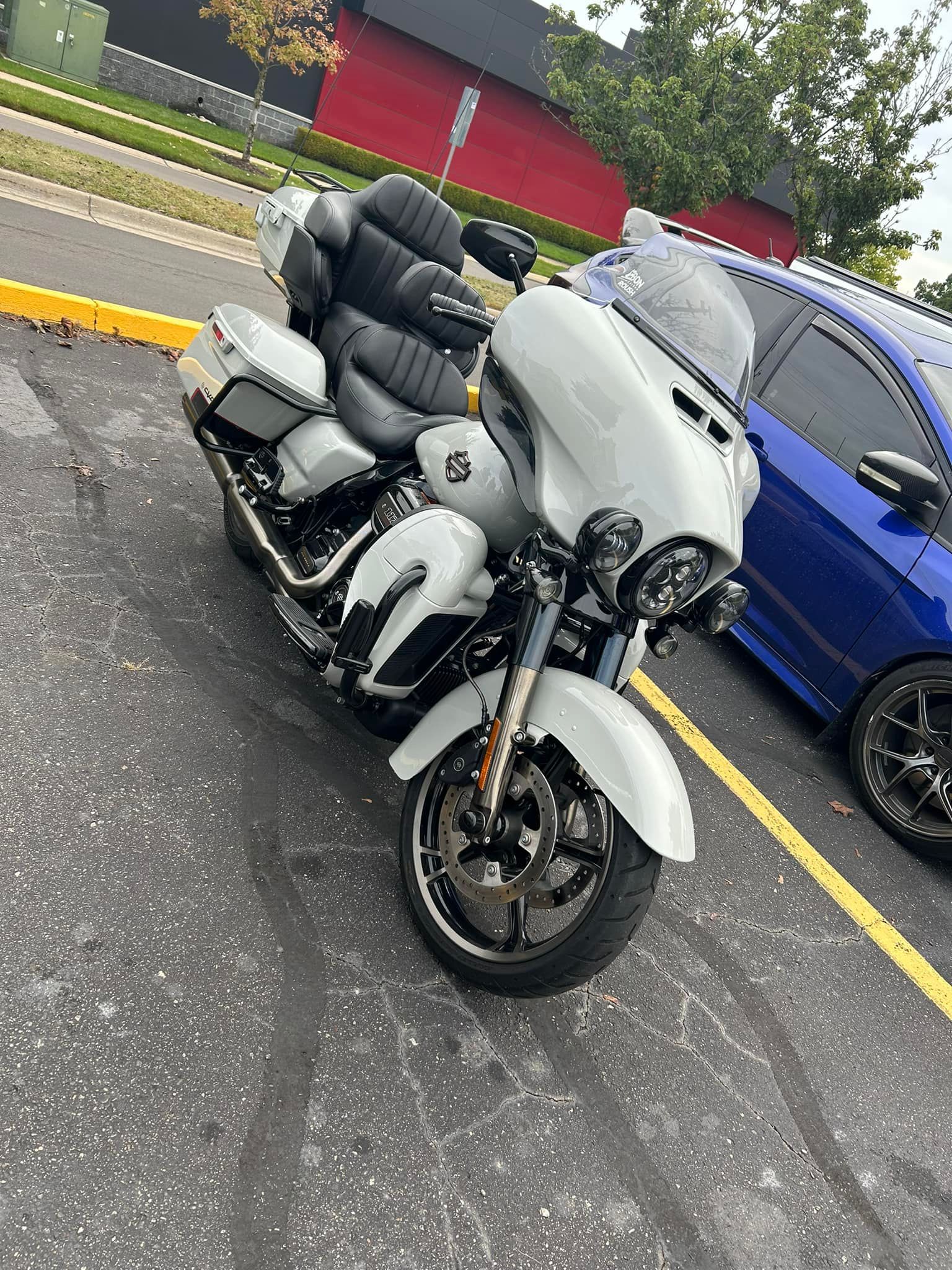 White touring motorcycle parked in a lot beside a blue car, with a red truck in the background.