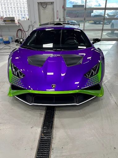 Purple and green Lamborghini in a garage, front view with black accents and a floor drain in front.