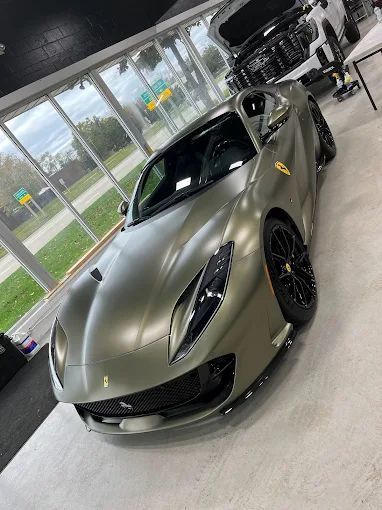 Matte olive-green sports car in a showroom with floor-to-ceiling windows
