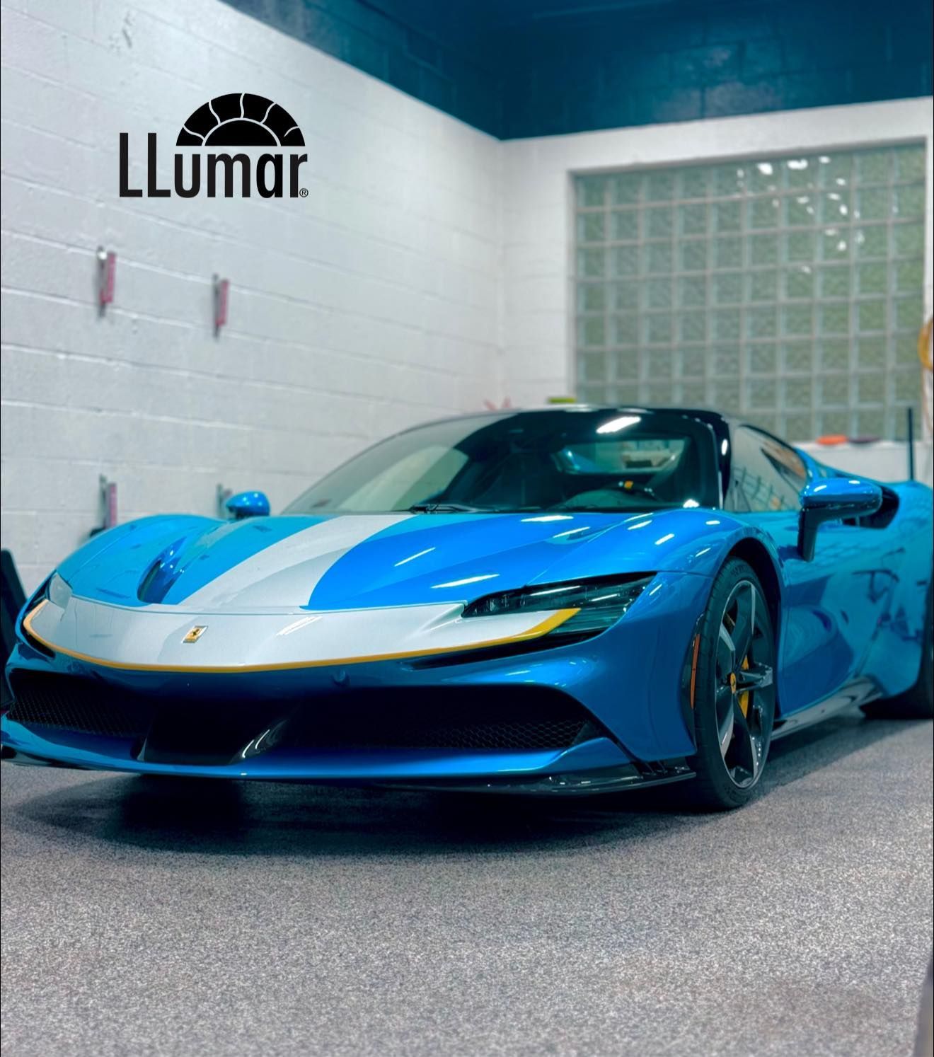 Blue sports car with white racing stripes parked indoors at a Lumar showroom