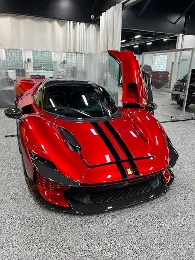 Red supercar with black racing stripes and one door raised, displayed indoors on a showroom floor