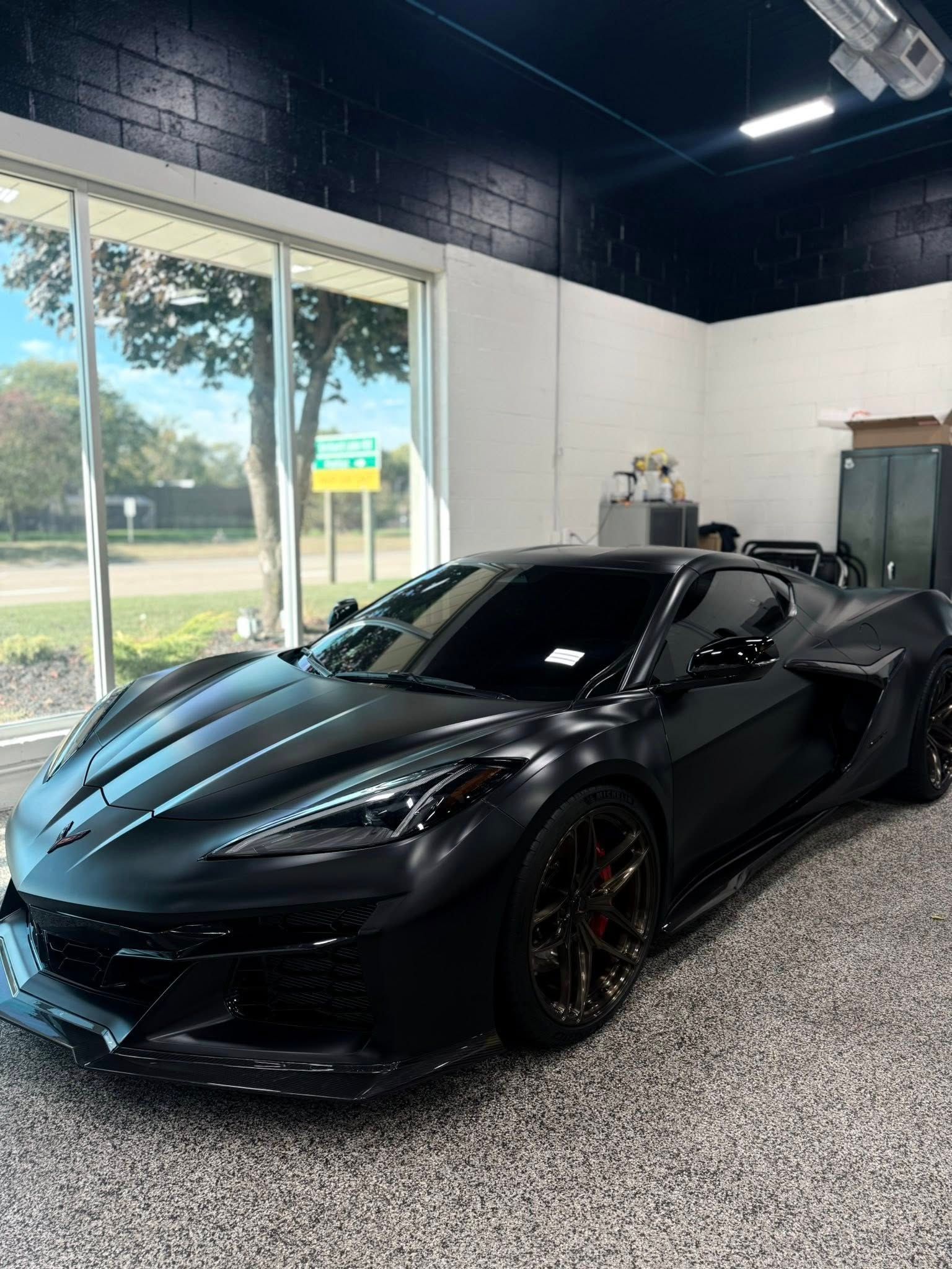 Black sports car parked inside a garage with large open doors and daylight visible outside
