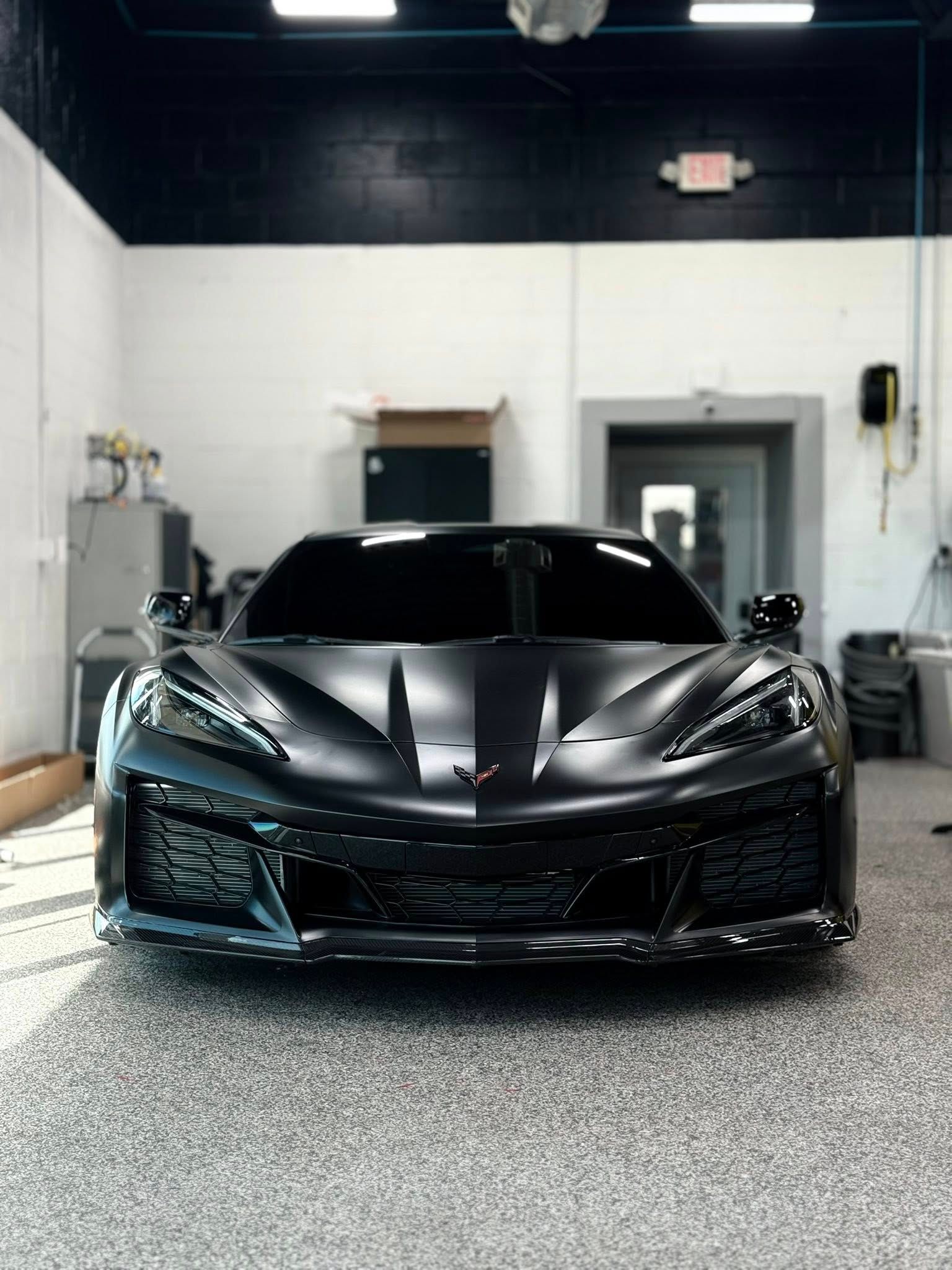 Black sports car parked indoors in a garage, front view with glossy finish.