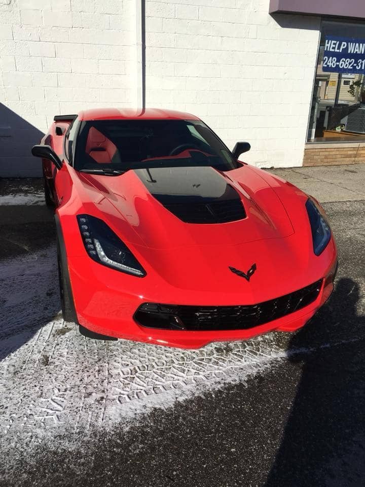 Red Chevrolet Corvette parked outside a building, bright red with black hood accents.