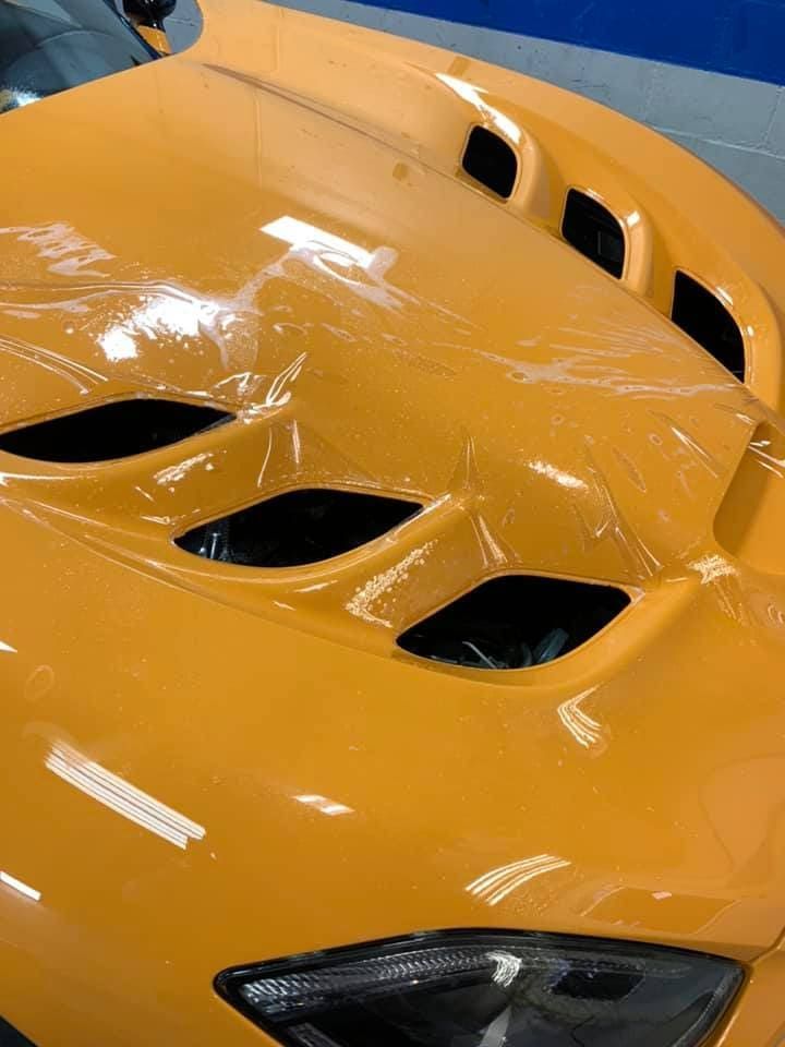 Close-up of an orange sports car hood with black vents and a glossy finish