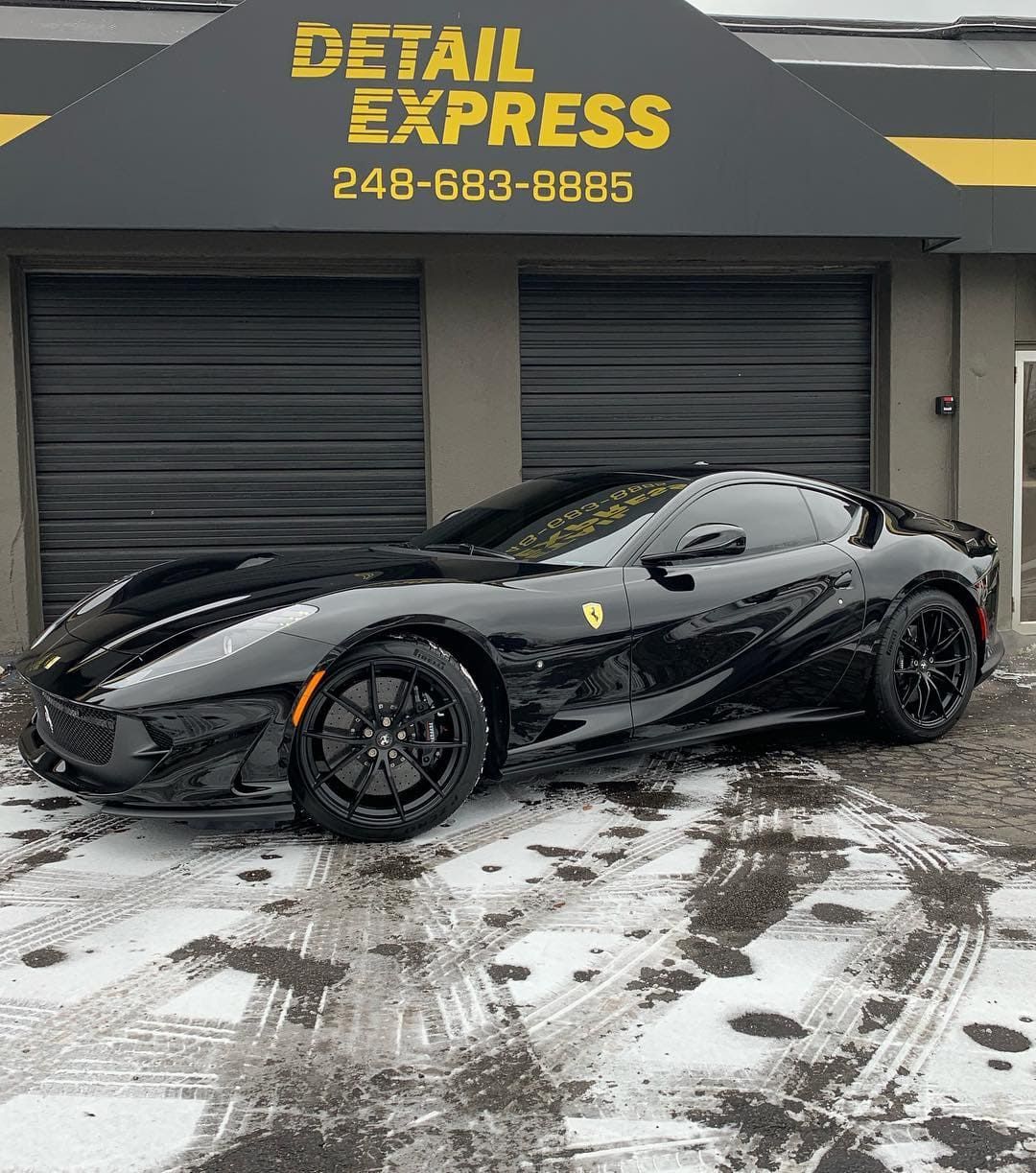 Black Ferrari parked outside Detail Express on a snowy day.