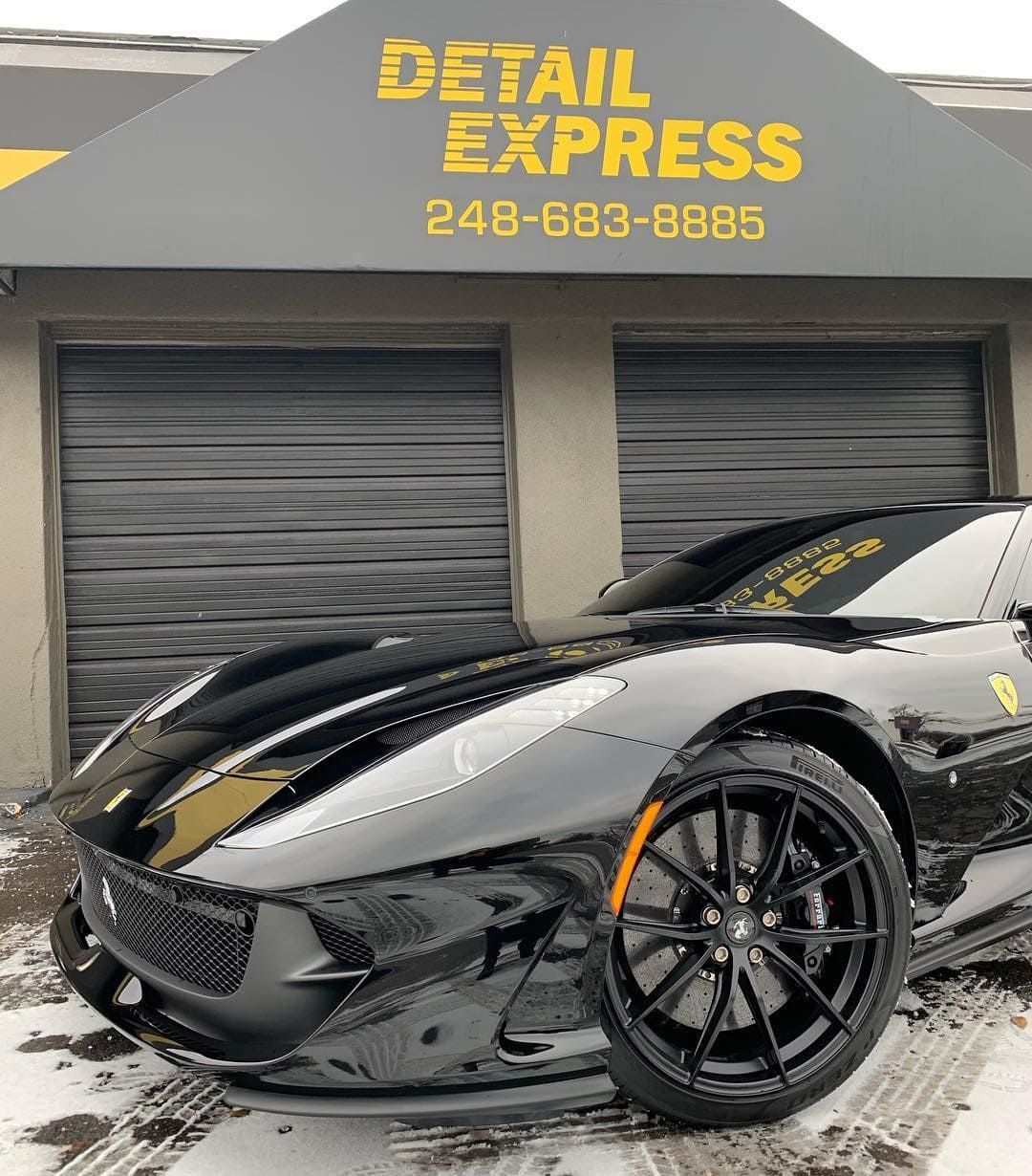 Black sports car parked outside Detail Express auto shop with wet pavement and gray garage doors
