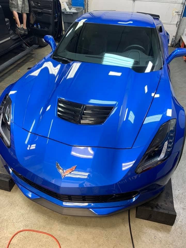 Bright blue sports car parked indoors, front view with hood vents and Corvette emblem