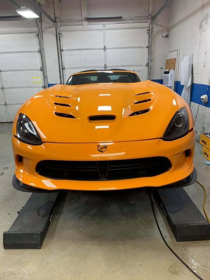 Orange sports car parked in a garage on ramps, front view.