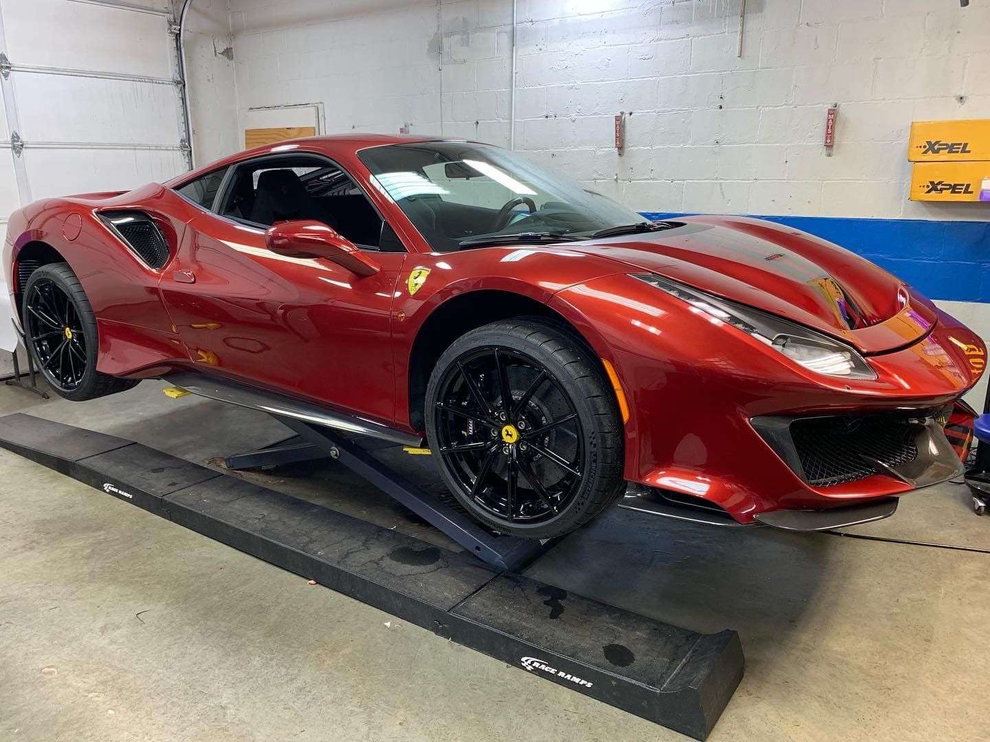 Red Ferrari sports car on a garage lift, viewed from the front-left side.