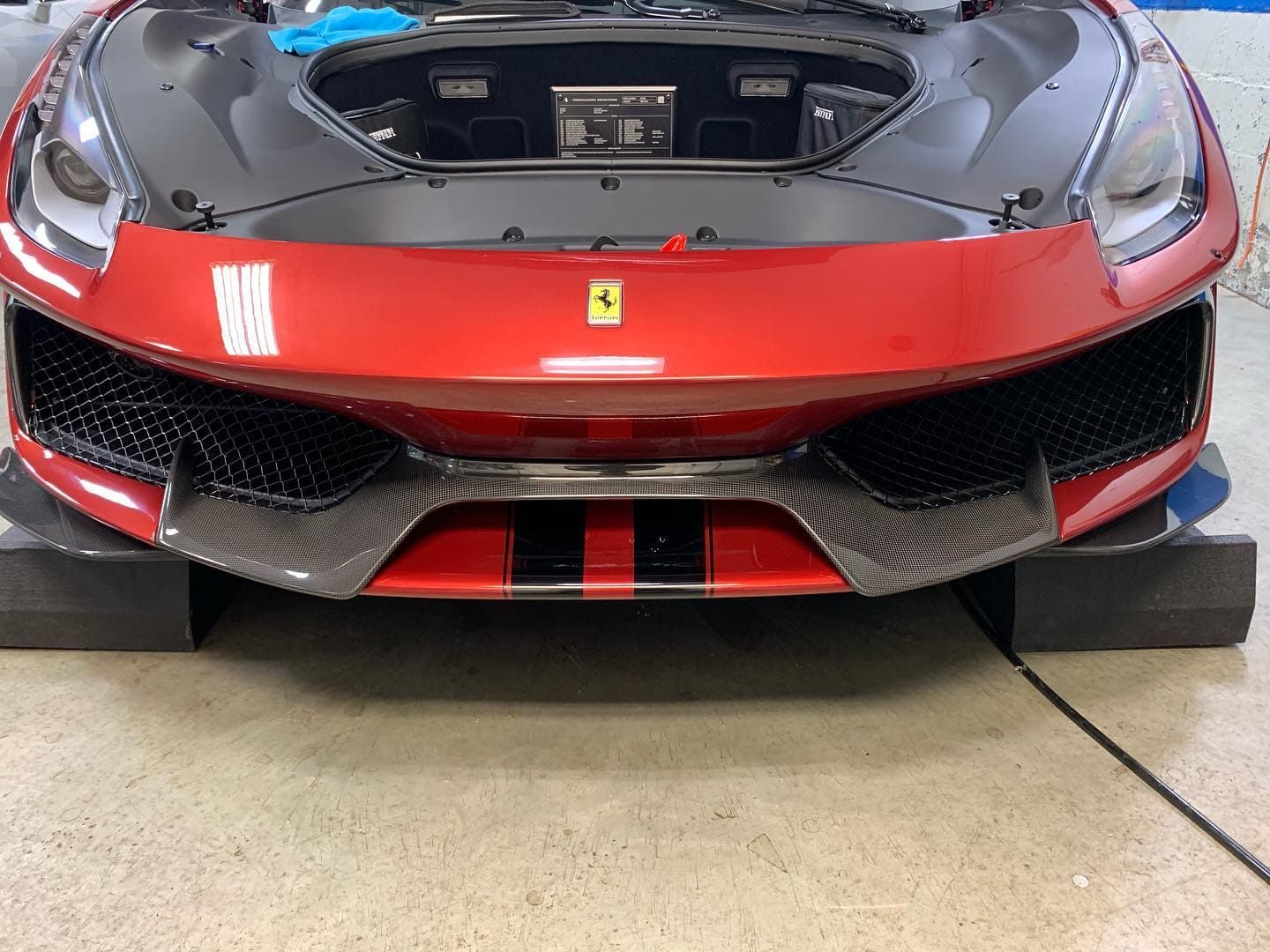 Front view of a red Ferrari sports car in a garage, with the hood open.