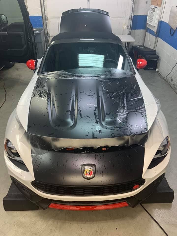 Silver sports car with black hood parked indoors, front view, wet with water droplets.