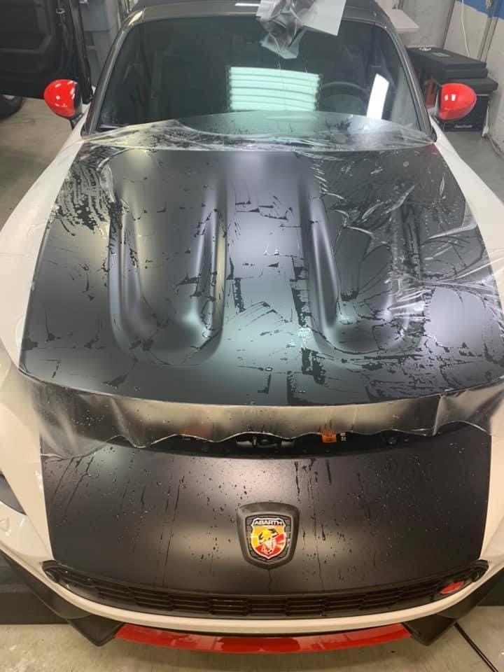 Black Porsche sports car with a water-covered windshield parked indoors, front view