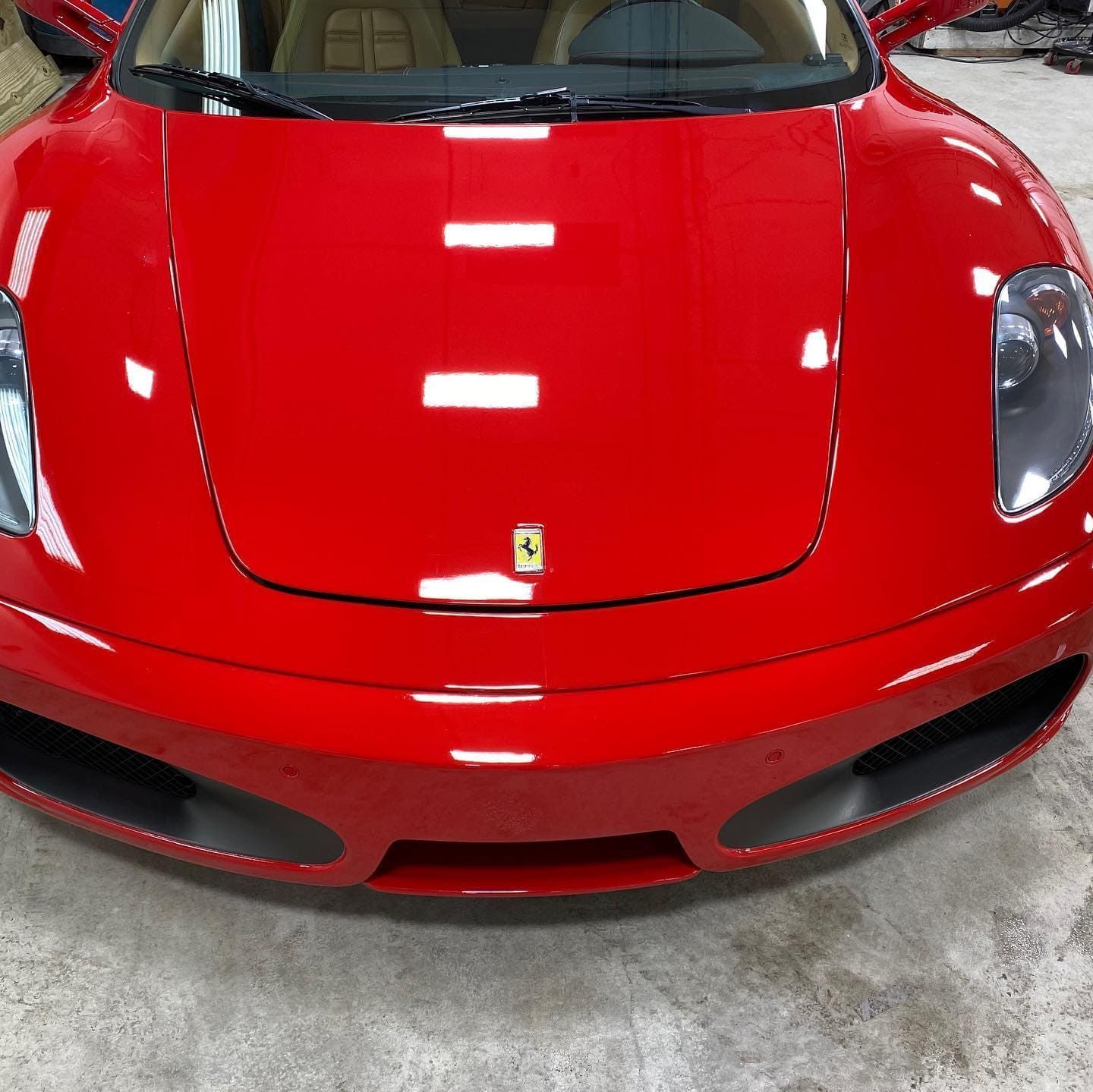 Red sports car front view, glossy finish, parked indoors on a concrete floor.