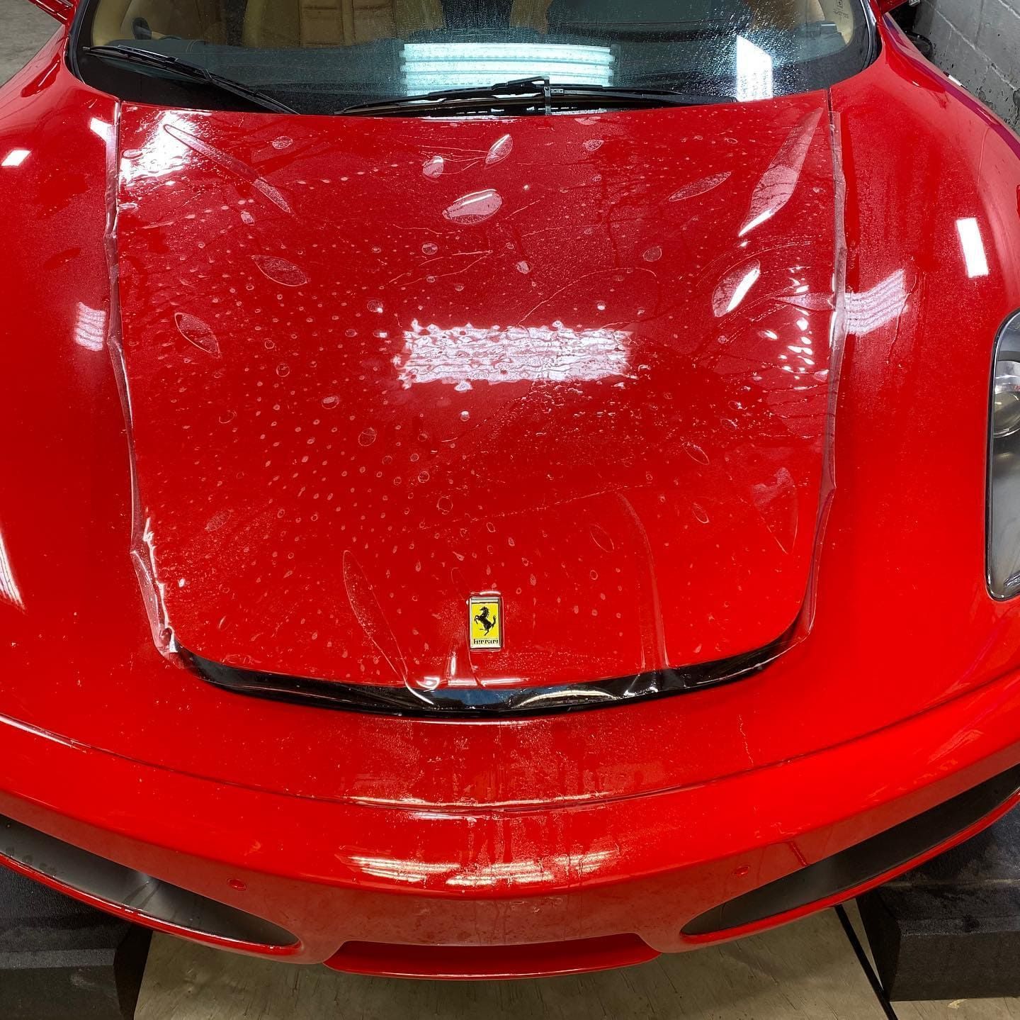 Red Ferrari sports car front hood in glossy red, photographed indoors under lights