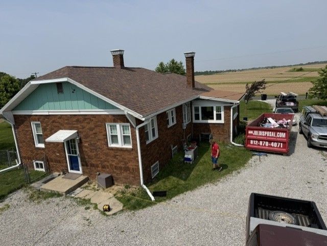 Brick house with teal trim beside a gravel drive and moving truck in a rural field setting