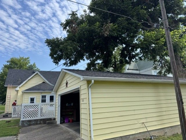 Yellow garage with open door beside a house, under a cloudy sky.