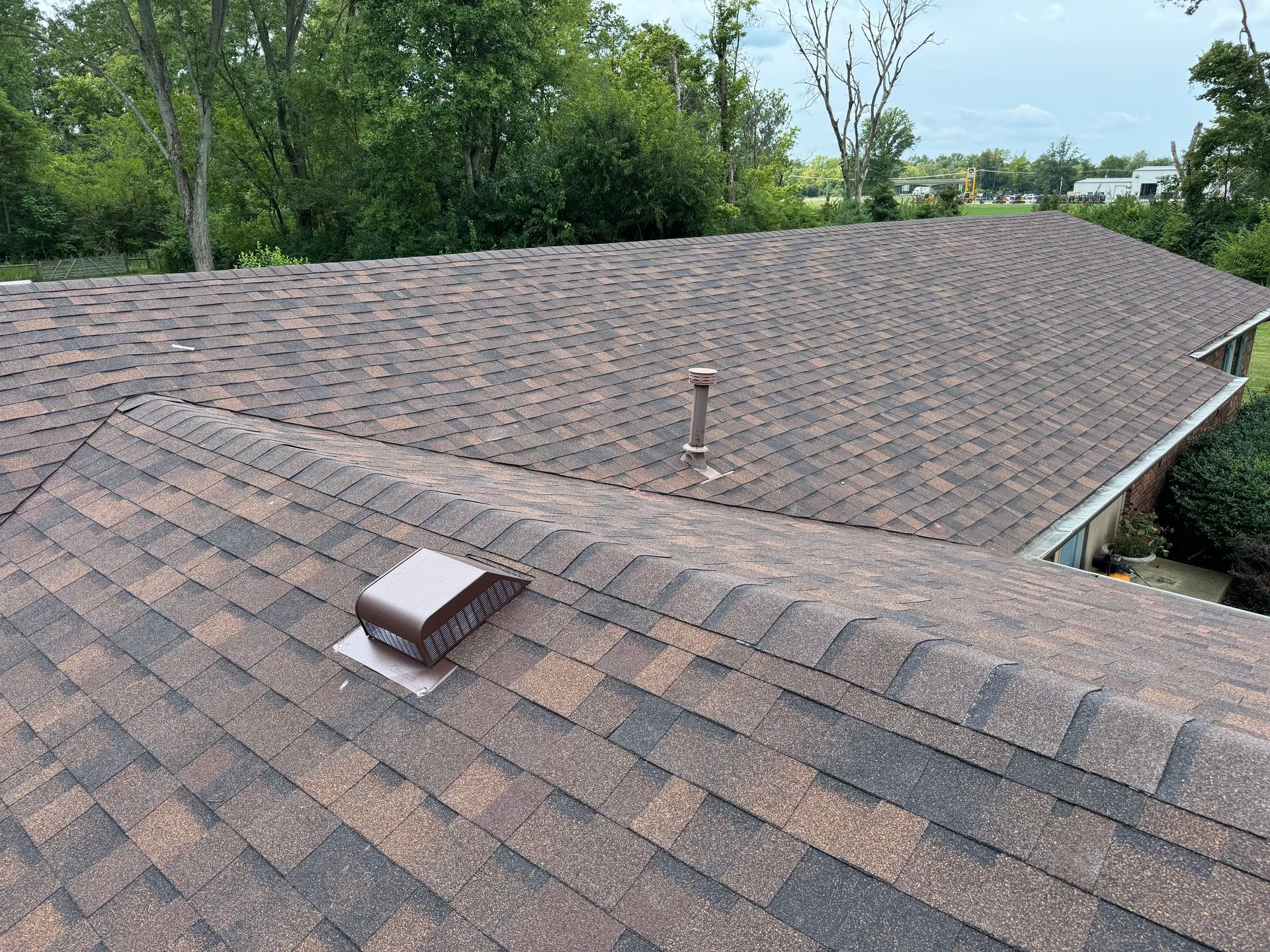 A roof with a vent on it and trees in the background.