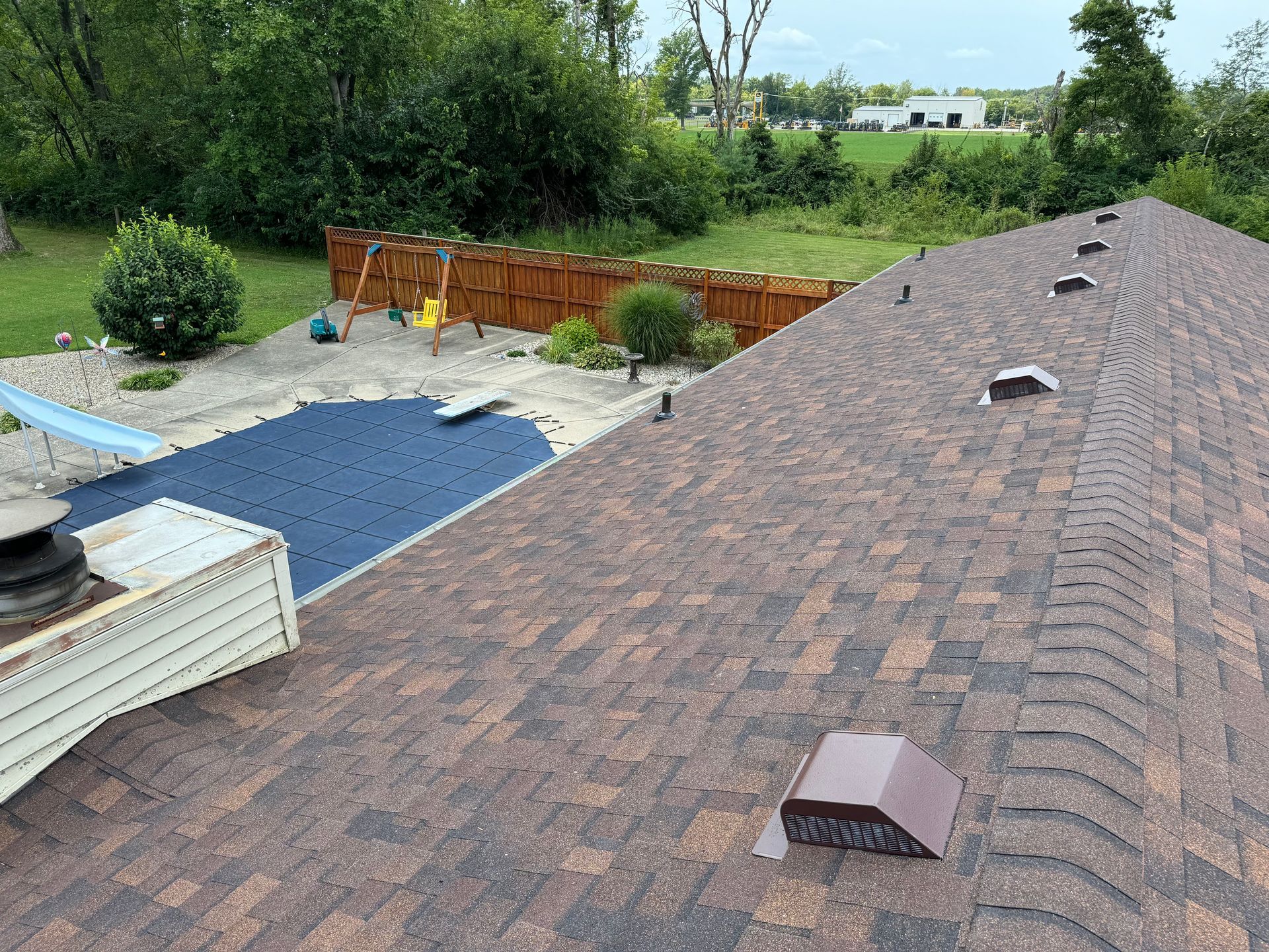 A roof with a pool in the background and a fence in the background.