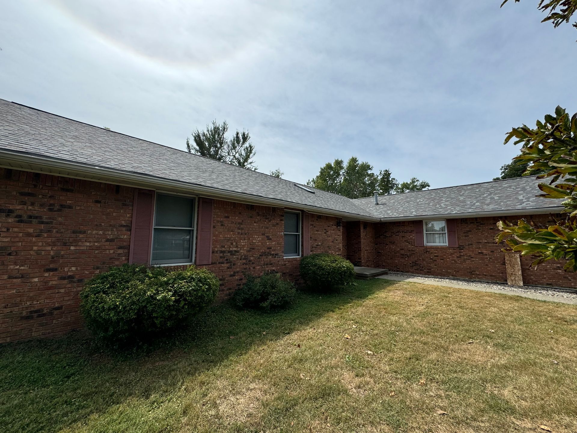 A brick house with a roof and a lot of grass in front of it.