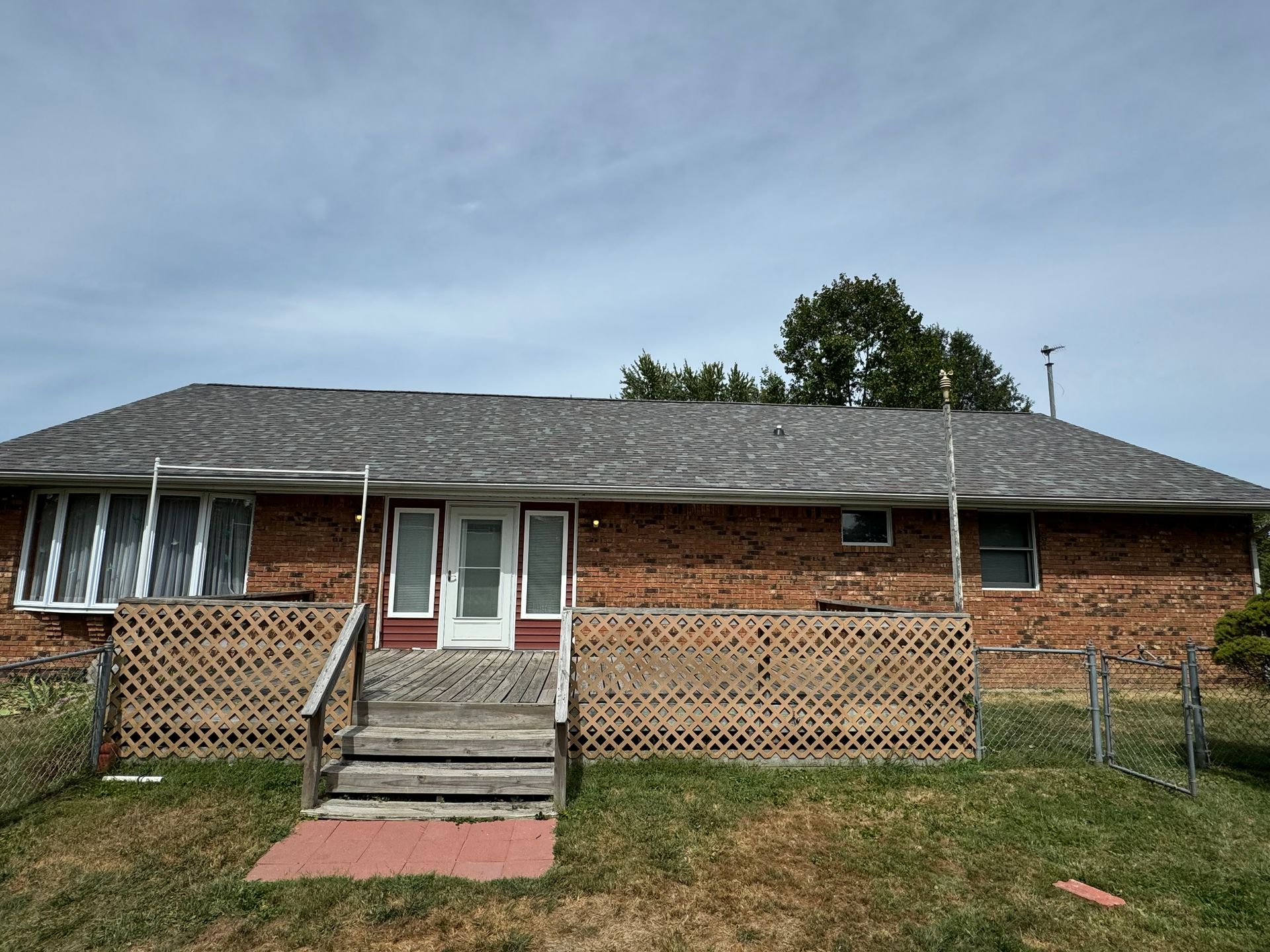 A brick house with a gray roof is sitting in the middle of a grassy field.